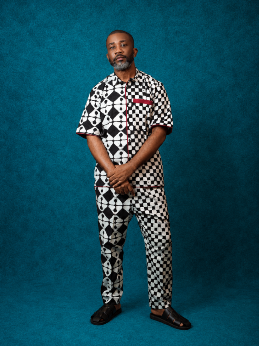 Model wearing an OBIDA black-and-white patterned shirt and trouser set against a teal studio backdrop.