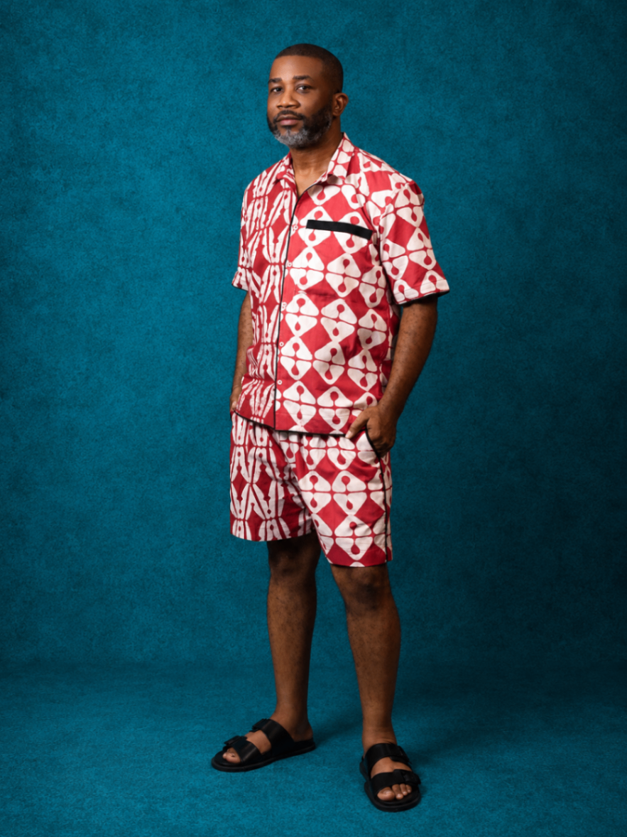 Model wearing an OBIDA red short-sleeve shirt and matching shorts against a teal studio backdrop.