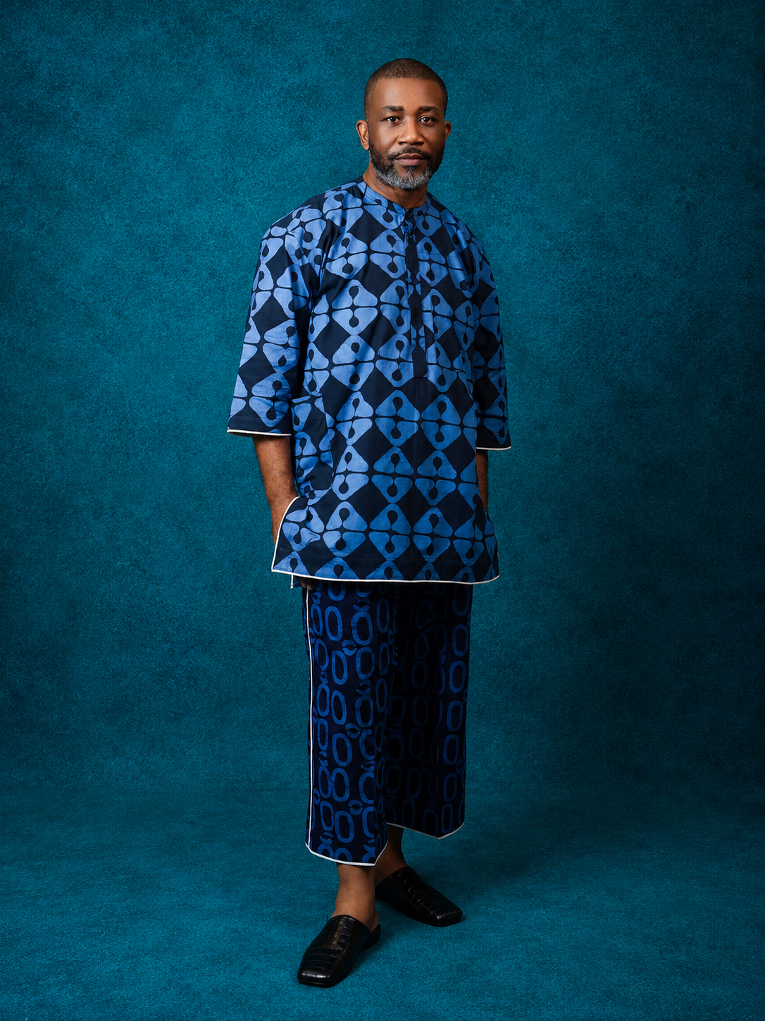 Model wearing an OBIDA blue patterned kaftan set against a teal studio backdrop.