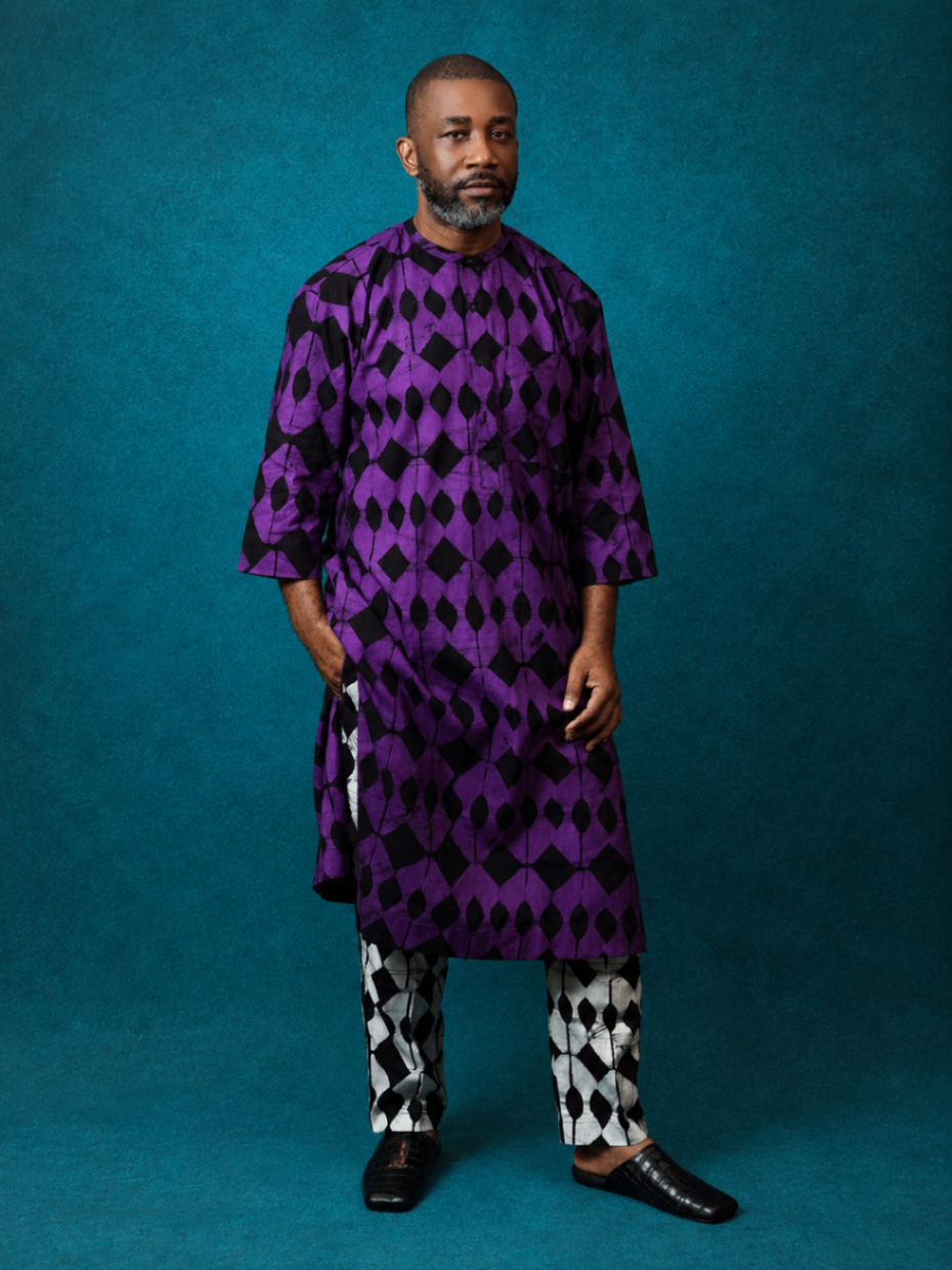 Model wearing an OBIDA purple kaftan set with contrasting trousers against a teal studio backdrop.